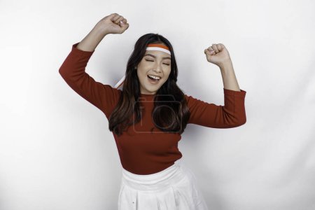 Photo for A young Asian woman with a happy successful expression wearing red top and flag headband isolated by white background. Indonesia's independence day concept. - Royalty Free Image