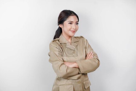 Photo for A young Asian woman in brown khaki uniform showing confident gesture by folding her arms. Indonesian government worker. - Royalty Free Image