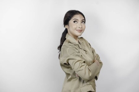 Téléchargez les photos : Une belle femme asiatique portant un uniforme marron souriant à la caméra, isolée par un fond blanc. Indonésie employés du gouvernement uniforme. - en image libre de droit