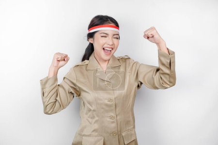 Photo for A young Asian government worker with a happy successful expression, wearing flag headband and khaki uniform isolated by white background. Indonesia's independence day concept. - Royalty Free Image