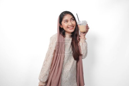 Lächelnde asiatische Muslimin im Kopftuchschleier-Hijab mit Kaffee in einer Plastikschale, die darauf wartet, dass Iftar getrunken wird. Ramadan-Konzept