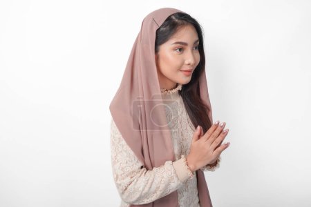 Smiling young Asian Muslim woman gesturing Eid Mubarak greeting from side view isolated over white background