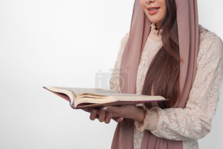 Retrato de cerca de una mujer musulmana asiática con velo de pañuelo en la cabeza hiyab sosteniendo y leyendo Al Corán sobre un fondo blanco aislado. Concepto Ramadán y Eid Mubarak.