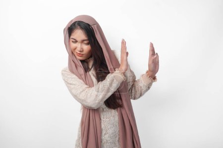 Young Asian Muslim woman wearing veil hijab gesturing a no rejection, refuse using hands and fingers, isolated by white background. Ramadan and Eid Mubarak concept