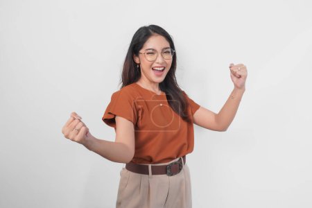 A young Asian woman wearing brown shirt and eyeglasses with a happy successful expression isolated by white background.