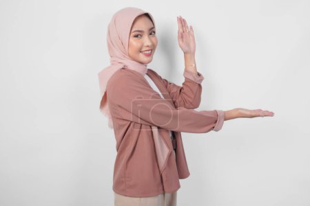 Glückliche junge asiatische Muslimin im Hijab präsentiert Kopierraum neben sich auf isoliertem weißem Hintergrund.