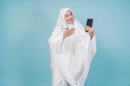 Joyeux jeune femme musulmane asiatique en robe de prière faire appel vidéo avec la famille ou un ami se sentir excité. Concept du Hadj.