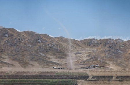 Real tornado in Peru, with farm field and mountains in the background.
