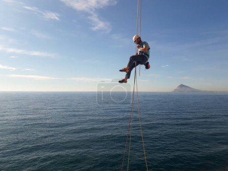 Foto de Escalador en las montañas españolas colgando de una roca sobre el mar. - Imagen libre de derechos