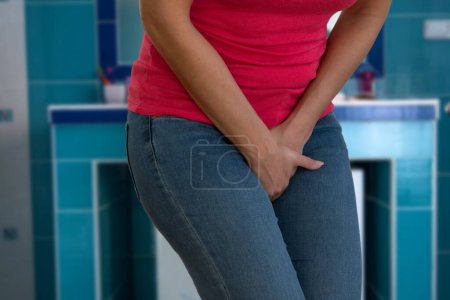Closeup of woman with hands holding her crotch in bathroom.