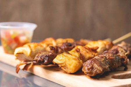 Foto de Brazilian churrasquinho. Kebabs with beef and chicken meat and bacon, known in Brazil by the name of churrasquinho. Wooden board, farofa and vinaigrette in the composition. Above view. - Imagen libre de derechos