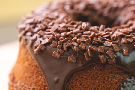 Chocolate cake with creamy chocolate sauce and decorated with chocolate sprinkles on a wooden board.
