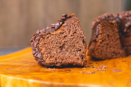 Photo for Chocolate cake with creamy chocolate sauce and decorated with chocolate sprinkles on a wooden board. Slice of cake. - Royalty Free Image