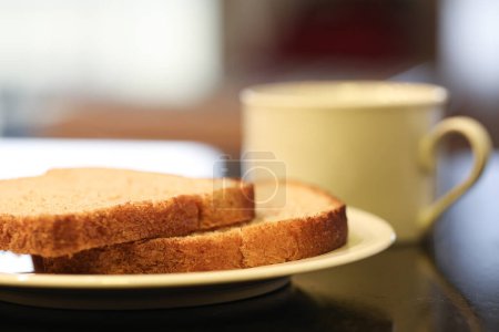 Téléchargez les photos : Deux tranches de pain de grains entiers sur une petite assiette blanche avec une tasse de thé en arrière-plan. Photographie macro. Fond de granit noir. - en image libre de droit