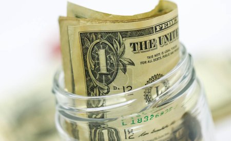 Foto de Billetes en dólares estadounidenses en una mesa de madera con un frasco de vidrio en macrofotografía. Concepto de ahorro. - Imagen libre de derechos