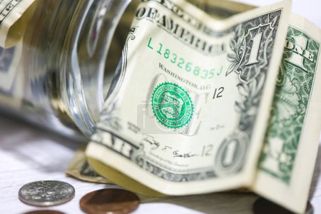 Foto de Billetes y monedas en dólares estadounidenses en una mesa de madera con un frasco de vidrio en macrofotografía. Concepto de ahorro. - Imagen libre de derechos