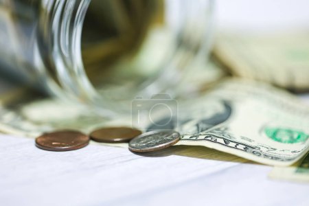 Foto de Billetes y monedas en dólares estadounidenses en una mesa de madera con un frasco de vidrio en macrofotografía. Concepto de ahorro. - Imagen libre de derechos