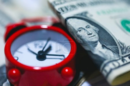 Foto de Billetes de dólar en una mesa de madera con un despertador rojo en la composición. Concepto de ahorro. - Imagen libre de derechos