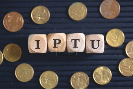 Photo for The acronym IPTU written on wooden cubes and coins on black background. - Royalty Free Image