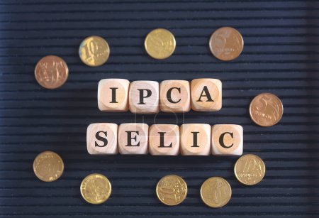 Foto de Las iniciales IPCA y SELIC escritas sobre cubos y monedas de madera sobre fondo negro. - Imagen libre de derechos