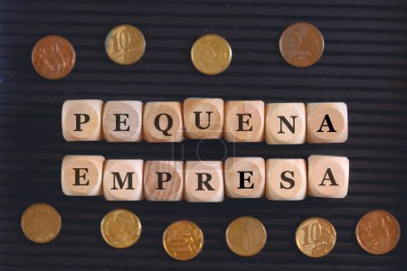 Foto de Inscripción PEQUEÑOS NEGOCIOS escritos sobre cubos y monedas de madera sobre fondo negro. - Imagen libre de derechos