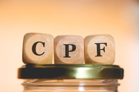 Photo for The abbreviation CPF written on wooden dice lying on top of a glass money-saving jar. Studio photo. - Royalty Free Image