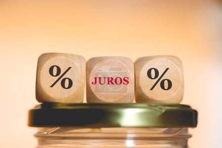 Photo for Percentage symbol and the acronym JUROS written on wooden cubes on top of a glass money-saving jar. Studio photo. - Royalty Free Image