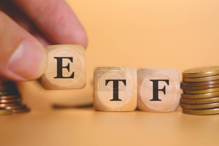 Close-up view of man forming acronym ETF for Exchange Traded Fund written on wooden cubes. Studio photo. 
