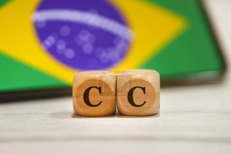 Photo for The acronym CC written on wooden cubes. A cell phone with the Brazilian flag on the screen in the composition. - Royalty Free Image