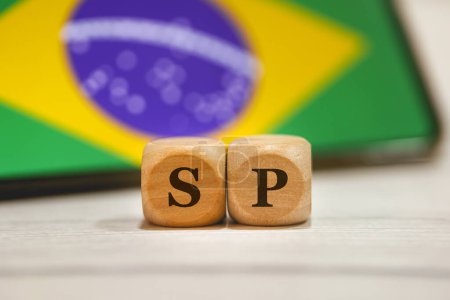 Foto de El acrónimo SP significa Sao Paulo, estado brasileño escrito en cubos de madera. Un teléfono celular con la bandera brasileña en la pantalla en la composición. - Imagen libre de derechos