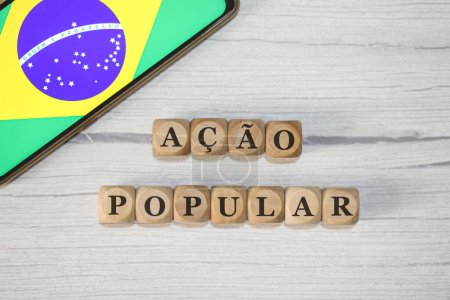 Foto de El texto ACCIÓN POPULAR en portugués brasileño escrito sobre cubos de madera. Un teléfono celular con la bandera brasileña que se muestra en la pantalla en la composición. - Imagen libre de derechos