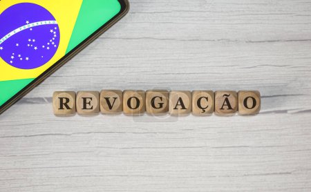 Foto de El texto Revocación en portugués brasileño escrito sobre cubos de madera. Un teléfono celular con la bandera brasileña que se muestra en la pantalla en la composición. - Imagen libre de derechos