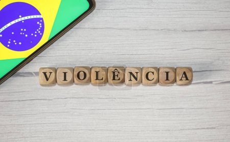 Photo for The text VIOLENCE in Brazilian Portuguese written on wooden cubes. A cell phone with the Brazilian flag being shown on the screen in the composition. - Royalty Free Image