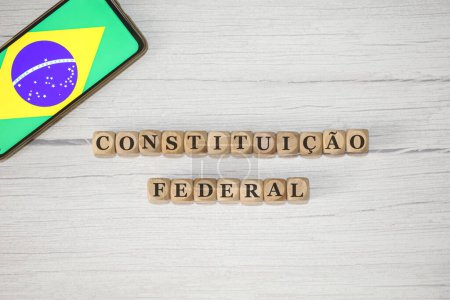 Foto de El texto CONSTITUCIÓN FEDERAL en portugués brasileño escrito sobre cubos de madera. Un teléfono celular con la bandera brasileña que se muestra en la pantalla en la composición. - Imagen libre de derechos