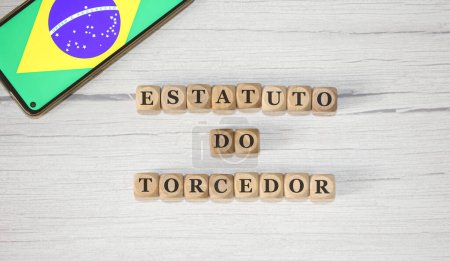 Foto de El texto ESTATUTOS DE FAN en portugués brasileño escrito sobre cubos de madera. Un teléfono celular con la bandera brasileña que se muestra en la pantalla en la composición. - Imagen libre de derechos