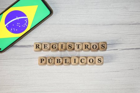 Photo for The text PUBLIC RECORDS in Brazilian Portuguese written on wooden cubes. A cell phone with the Brazilian flag being shown on the screen in the composition. - Royalty Free Image