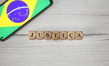Foto de El texto JUSTICIA en portugués brasileño escrito sobre cubos de madera. Un teléfono celular con la bandera brasileña que se muestra en la pantalla en la composición. - Imagen libre de derechos