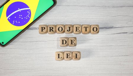 Photo for The text BILL in Brazilian Portuguese written on wooden cubes. A cell phone with the Brazilian flag being shown on the screen in the composition. - Royalty Free Image