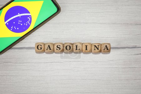 Téléchargez les photos : Le texte GASOLINE en portugais brésilien écrit sur des cubes de bois. Un téléphone portable avec le drapeau brésilien affiché à l'écran dans la composition. - en image libre de droit