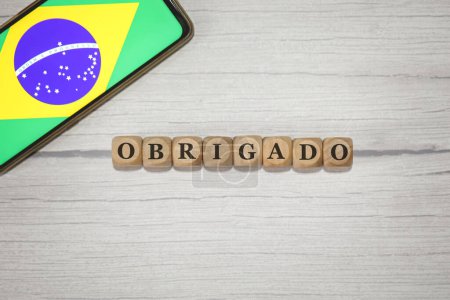 Foto de El texto GRACIAS en portugués brasileño escrito sobre cubos de madera. Un teléfono celular con la bandera brasileña que se muestra en la pantalla en la composición. - Imagen libre de derechos