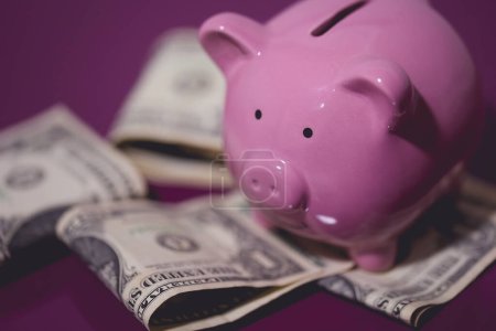 Foto de Una alcancía y billetes de dólar en un mueble de madera púrpura. Concepto financiero. - Imagen libre de derechos