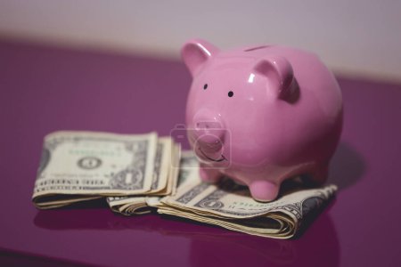 Foto de Una alcancía y billetes de dólar en un mueble de madera púrpura. Concepto financiero. - Imagen libre de derechos
