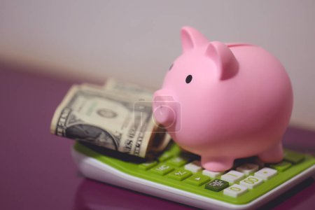 Una alcancía encima de una calculadora con billetes de dólar. Concepto de economía y finanzas.