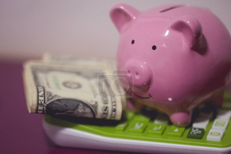 Foto de Una alcancía encima de una calculadora con billetes de dólar. Concepto de economía y finanzas. - Imagen libre de derechos