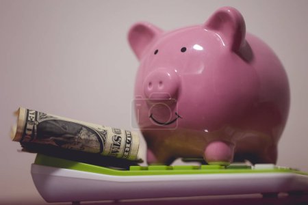Foto de Una alcancía encima de una calculadora con billetes de dólar. Concepto de economía y finanzas. - Imagen libre de derechos