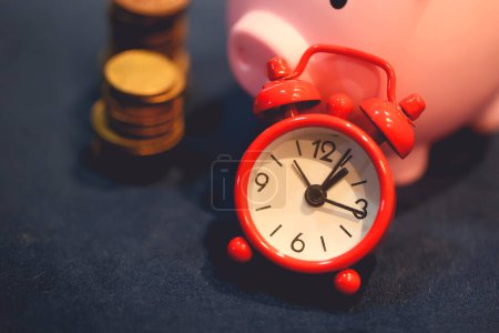 Photo for Close-up view of piggy bank with coins and alarm clock. Finance and time concepts. - Royalty Free Image