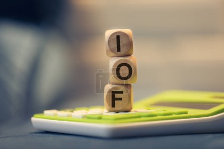 Foto de El acrónimo IOF para el Impuesto de Operaciones Financieras en portugués brasileño escrito en cubos de madera. Una calculadora en la composición. - Imagen libre de derechos