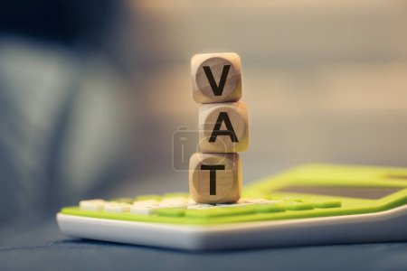 Photo for The acronym VAT for Value-Added Tax written on wooden cubes. A calculator in the composition. - Royalty Free Image