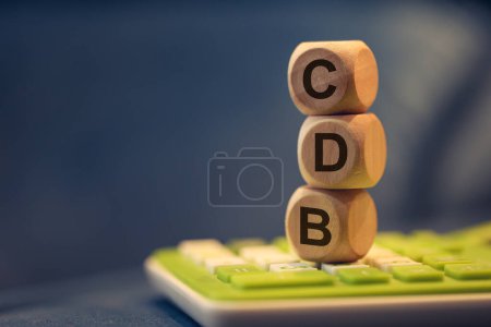 Foto de El acrónimo CDB para Certificado de Depósito Bancario en portugués brasileño escrito en cubos de madera. Una calculadora en la composición. - Imagen libre de derechos
