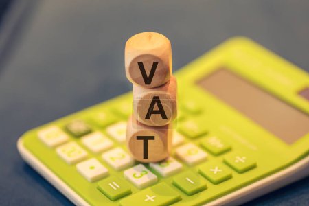 Das Akronym VAT für Mehrwertsteuer, geschrieben auf Holzwürfel. Ein Taschenrechner in der Zusammensetzung. 